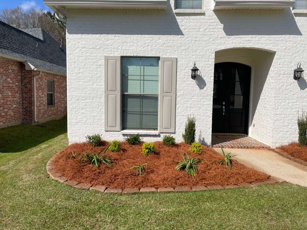 New red mulch landscaping bed with plants in front of a home
